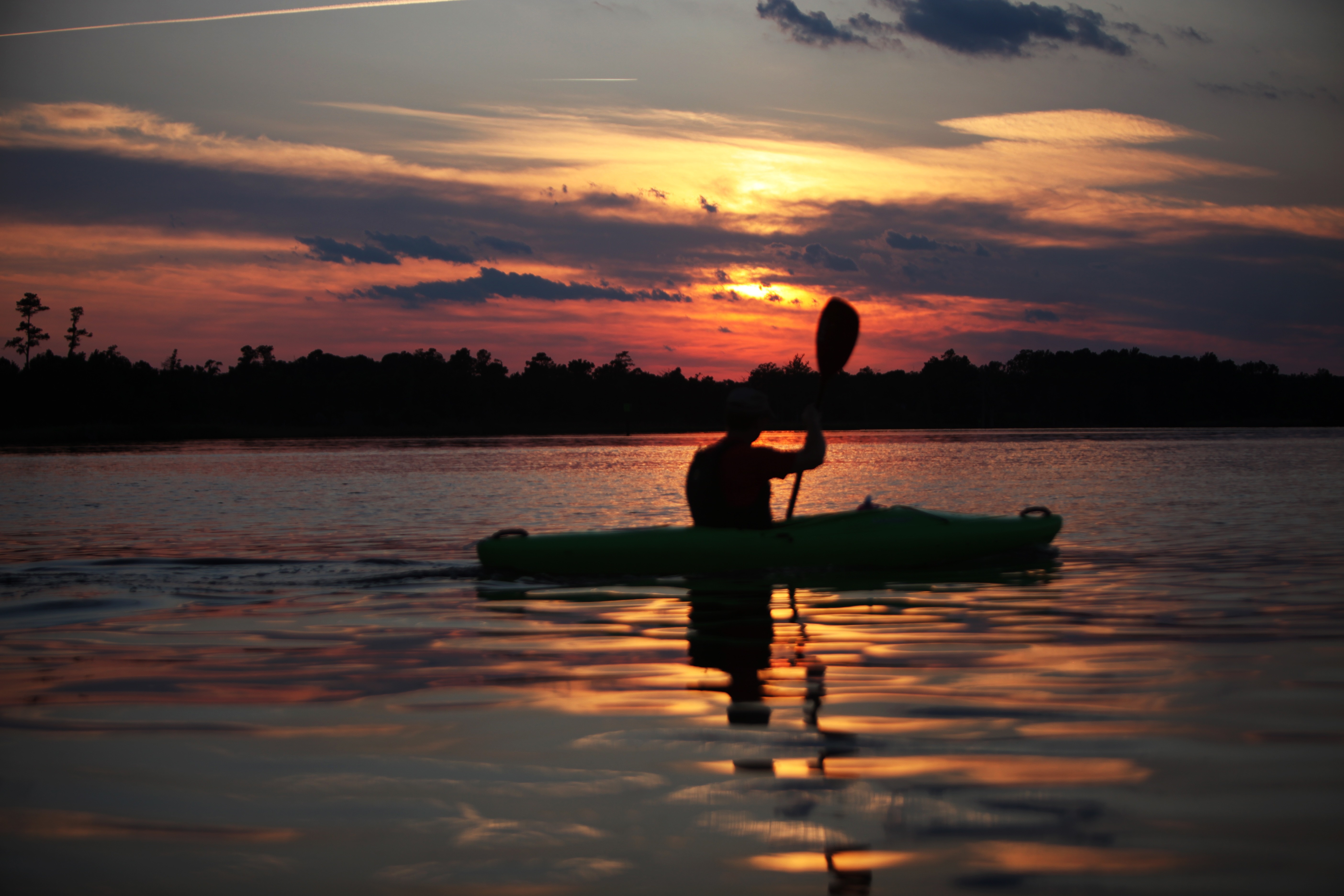silhouette of man riding on canoe boat holding paddle during golden hour