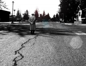 grayscale photo of man standing on gray concrete pavement thumbnail