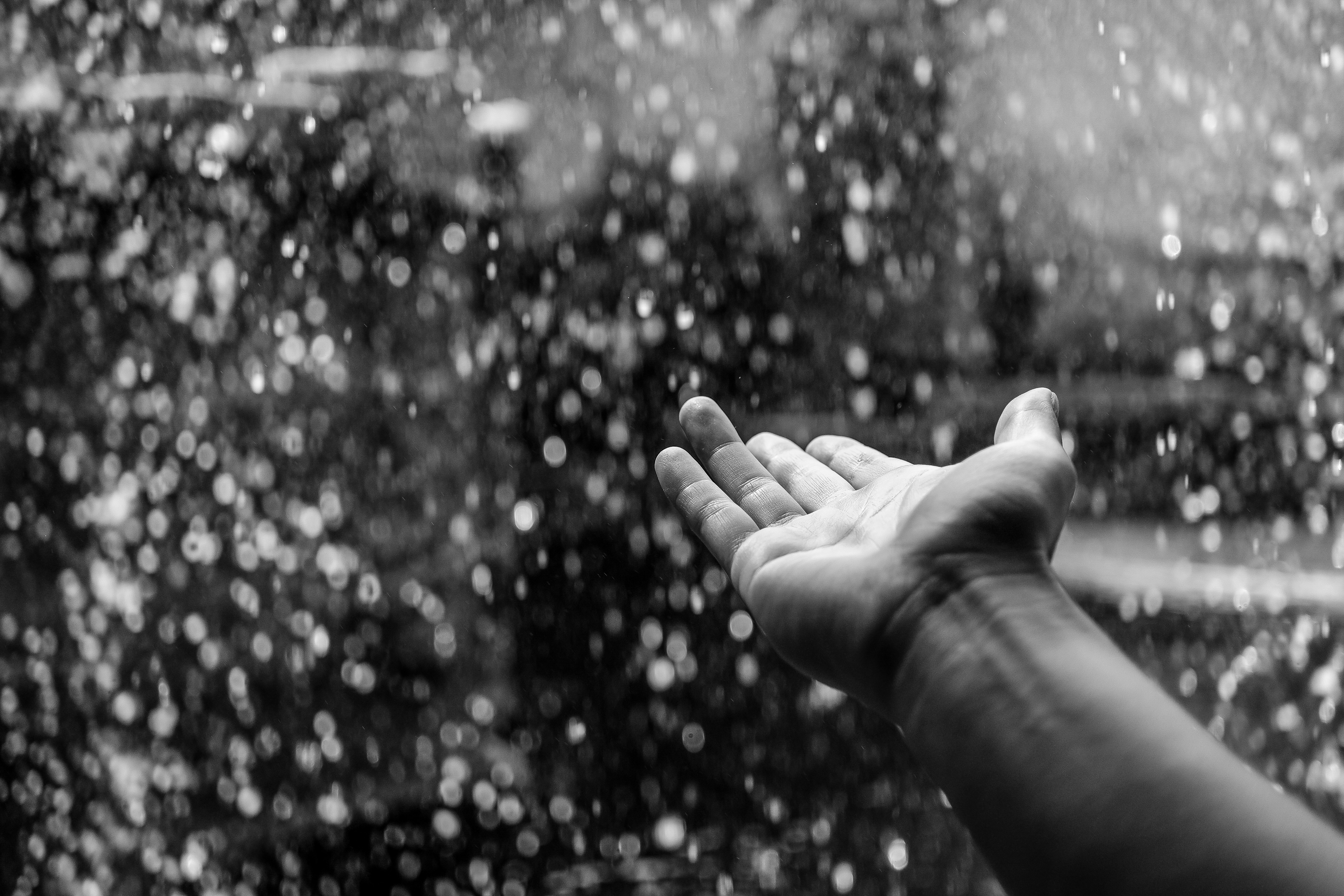 grey scale photo of human hand under the rain