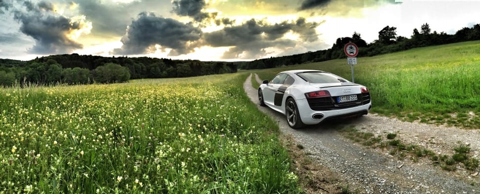 white sports coupe on gray ground surrounded with green fields at daytime preview