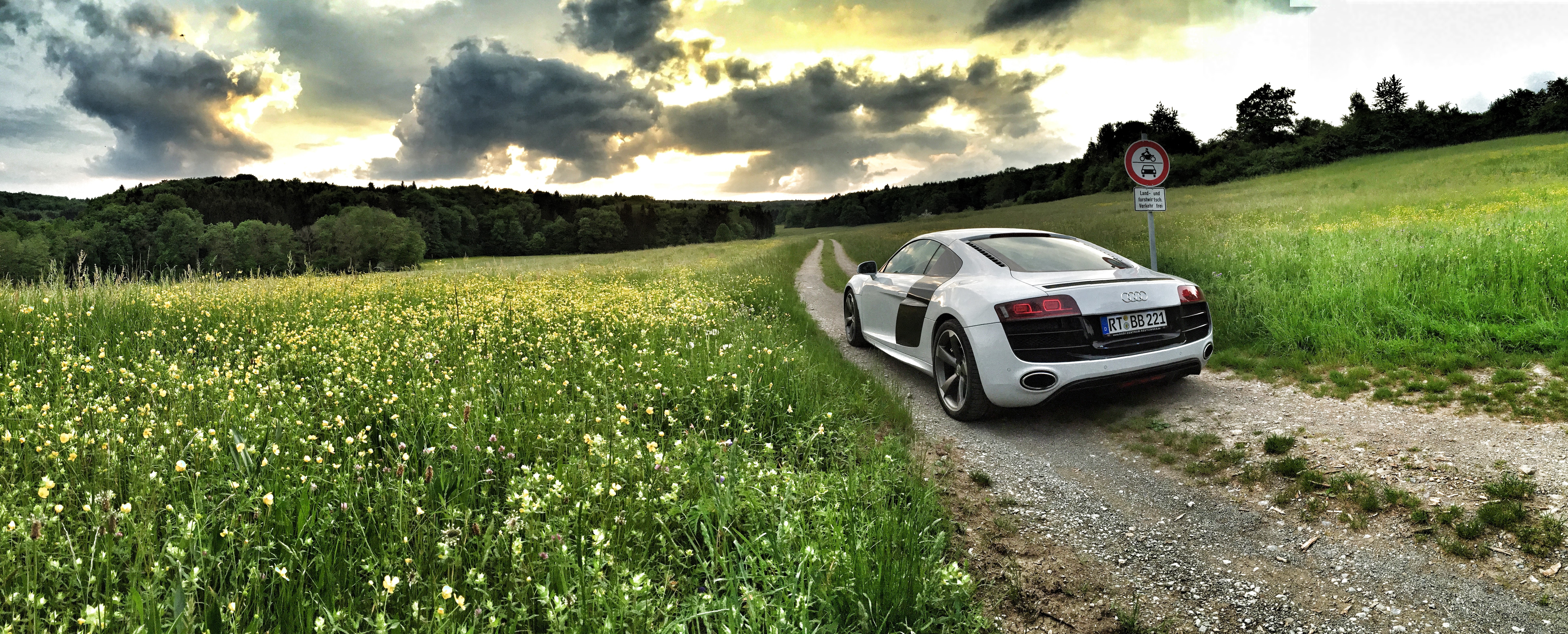 white sports coupe on gray ground surrounded with green fields at daytime