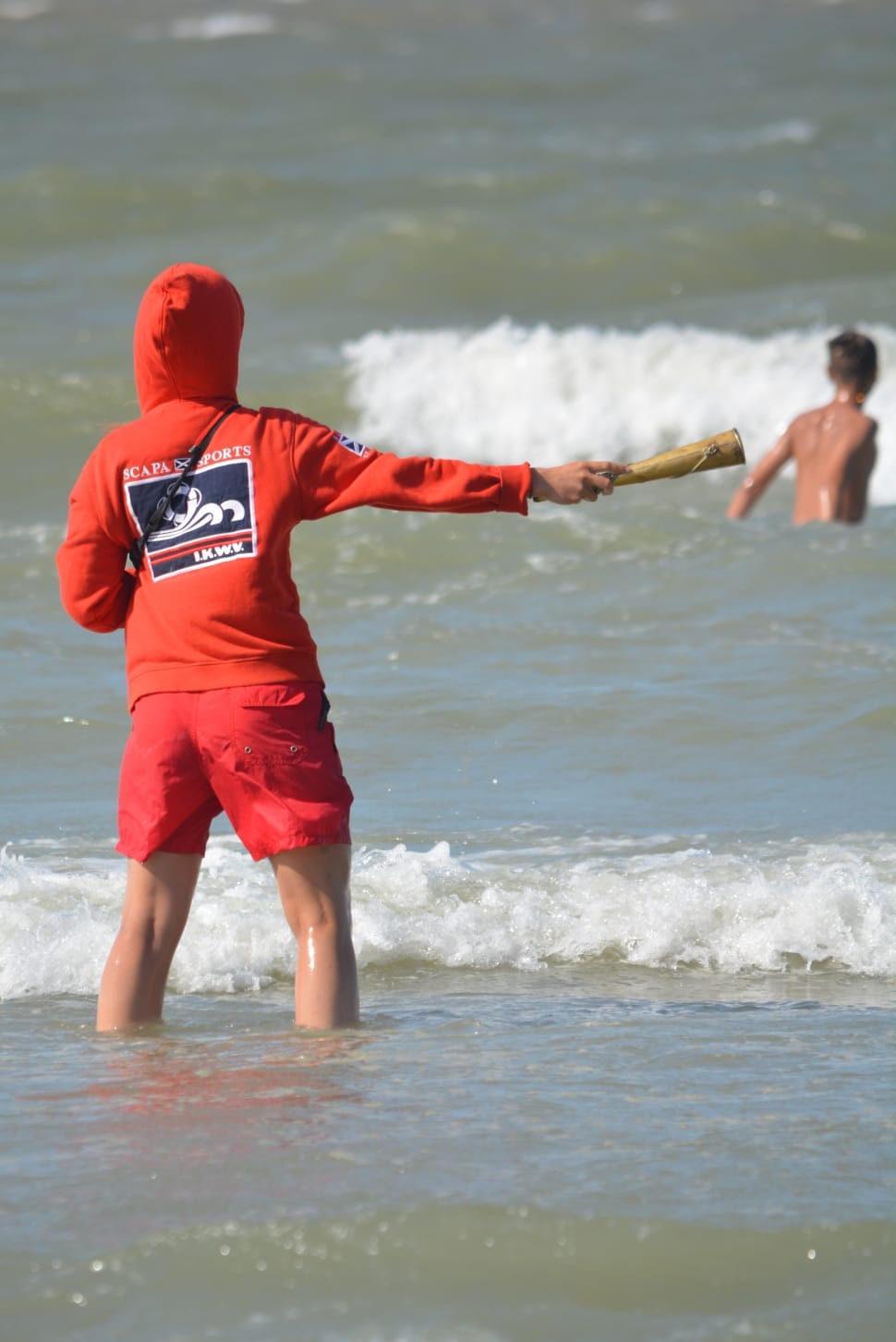 person wearing orange zip-up hoodie and red shorts in the ocean preview
