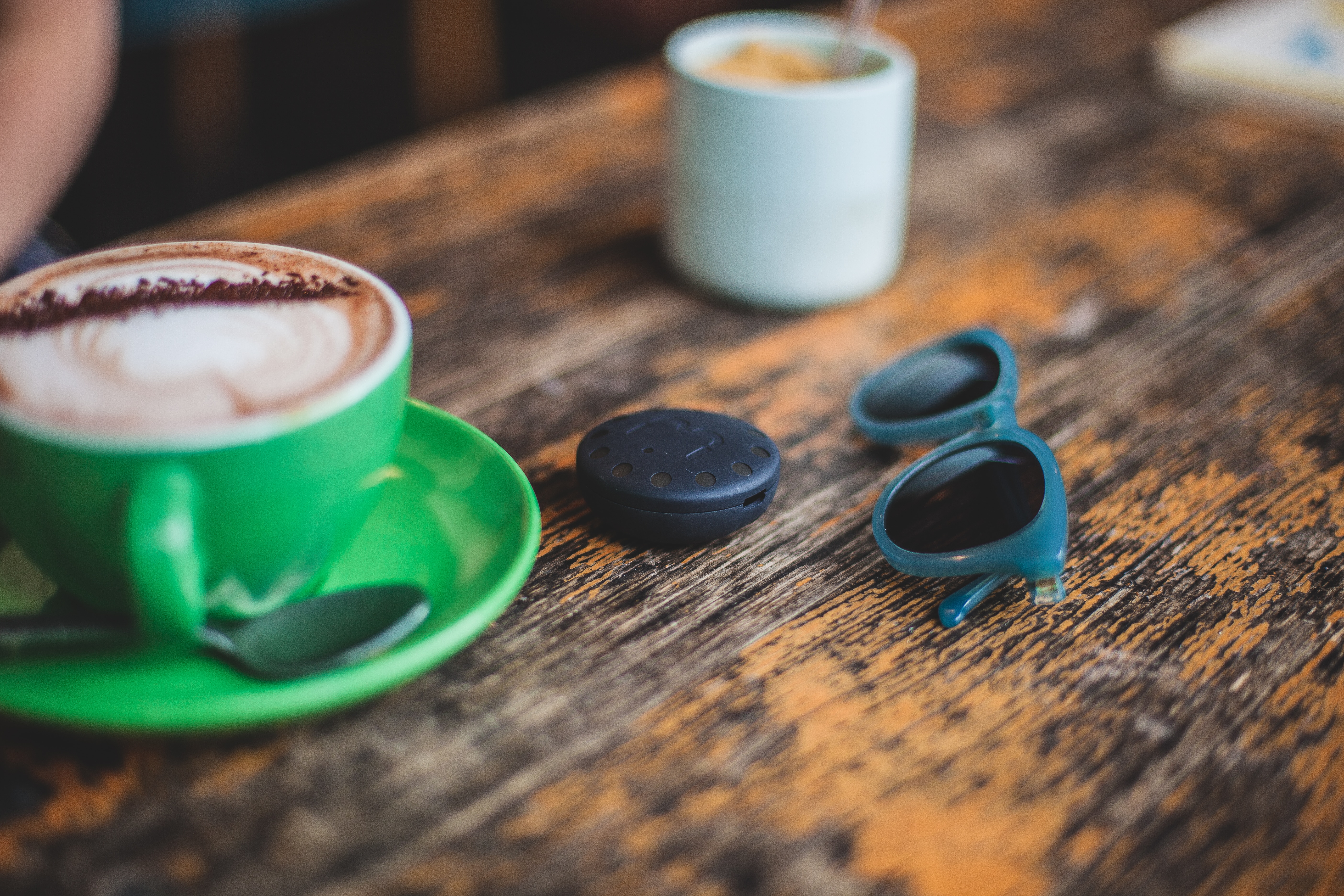 blue frame black lens sunglasses beside black round plastic container and green ceramic teacup filled with cappuccino
