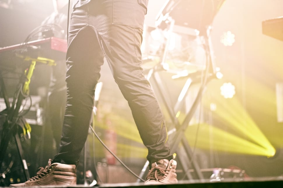 man in grey skinny pants and grey leather lace up sneakers standing on concert stage preview