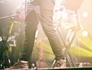 man in grey skinny pants and grey leather lace up sneakers standing on concert stage thumbnail