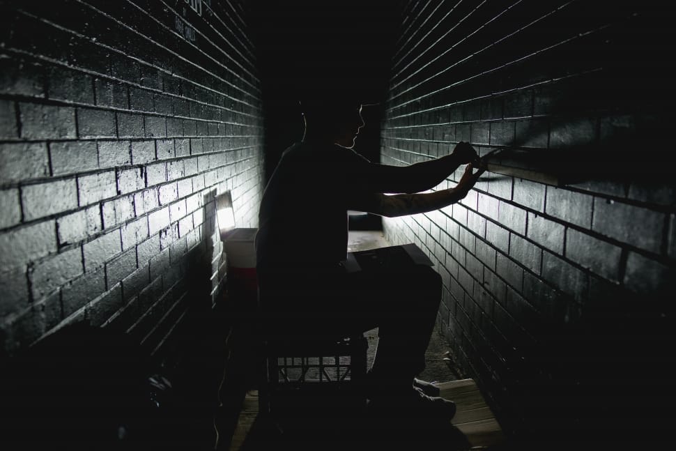 silhouette photograph of man sitting on crate while fixing the wall preview