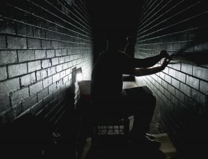 silhouette photograph of man sitting on crate while fixing the wall thumbnail