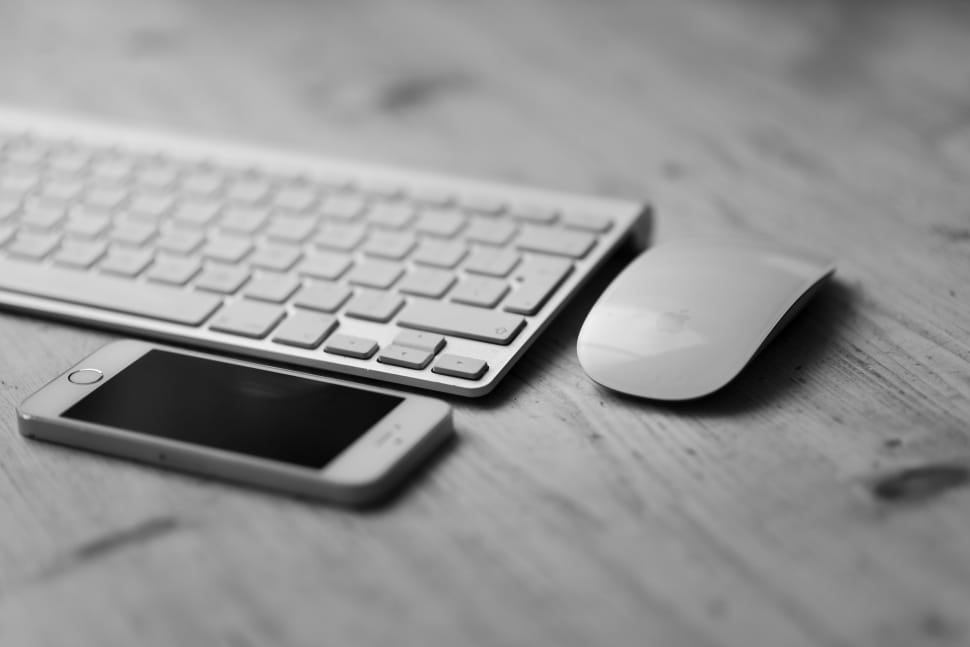 silver iphone 5es, apple magic mouse, and computer keyboard on top of wooden table preview
