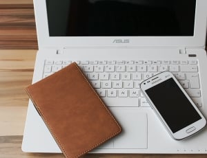 white Samsung android smartphone and leather wallet on white Asus laptop turned off thumbnail