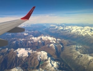 red and gray airplane wings with aerial view photo of snowy mountains thumbnail