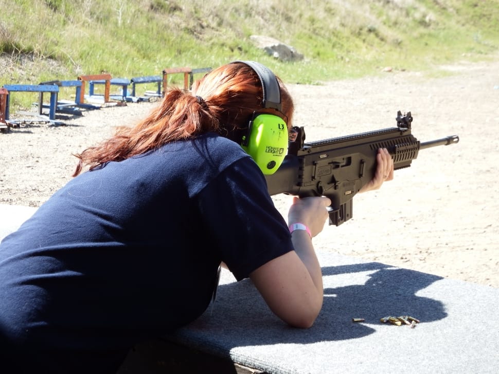 woman wearing blue t-shirt and green earmuffs holding rifle preview