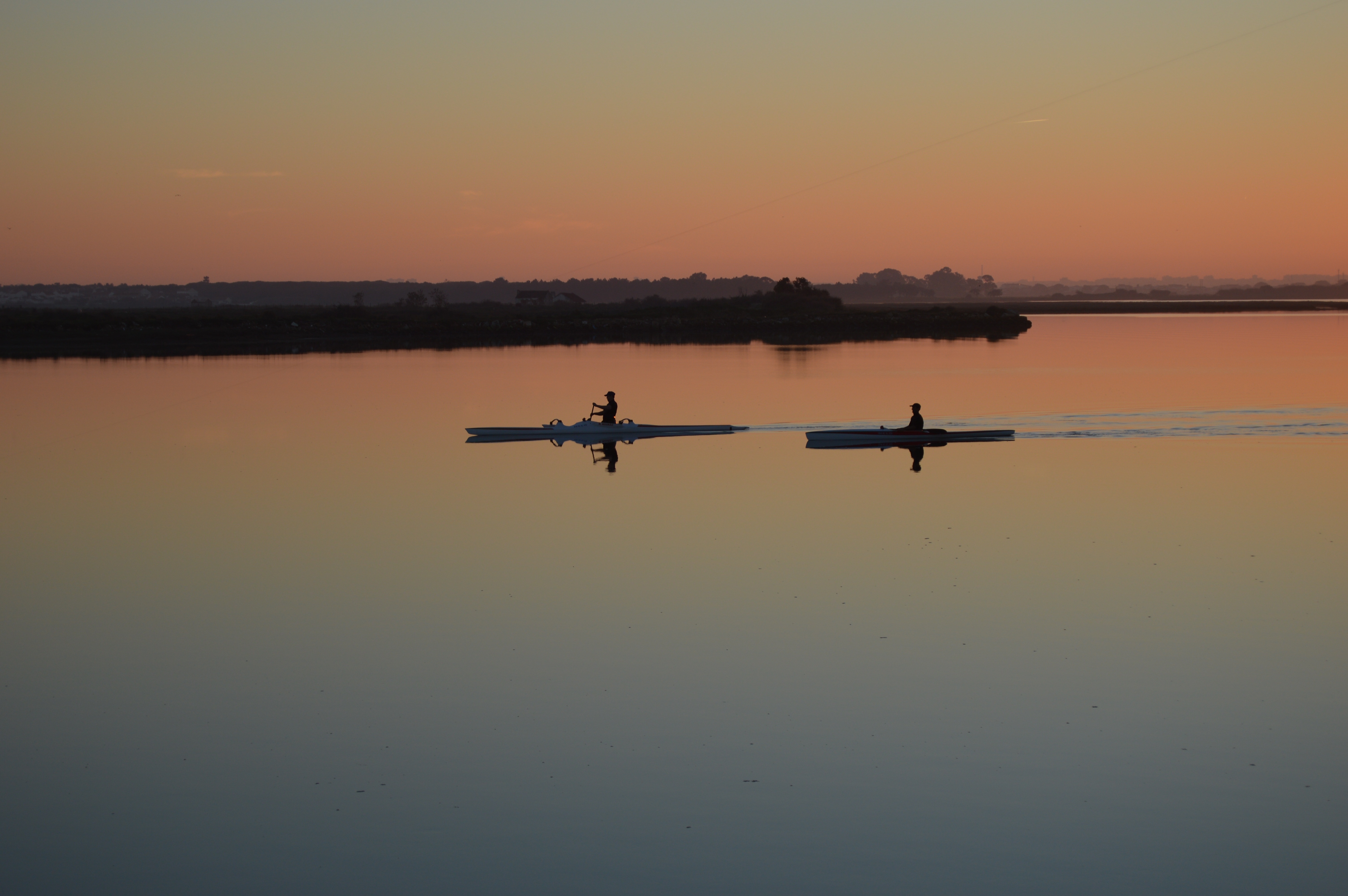 2 person rowing a boat at sunset