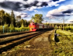 red steel train on rails during daytime thumbnail