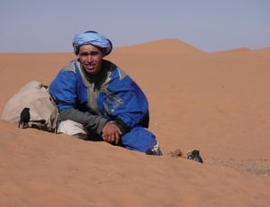 man wearing a blue turban and blue windbreaker in the middle of a desert thumbnail
