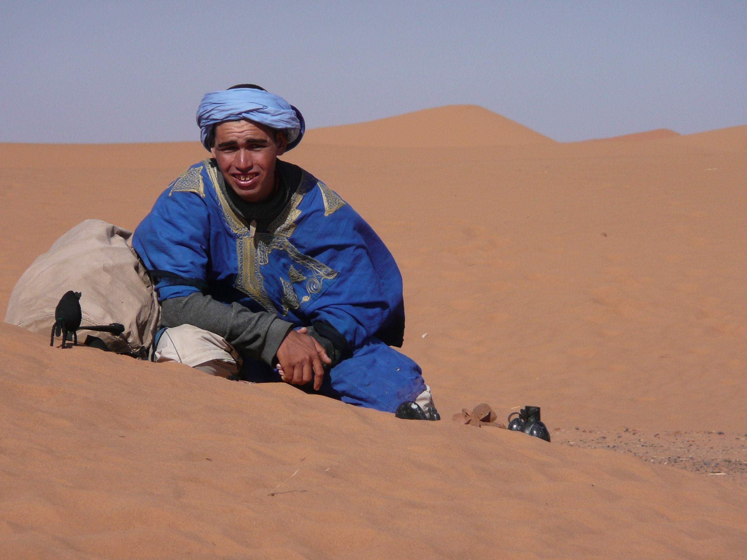 man wearing a blue turban and blue windbreaker in the middle of a desert