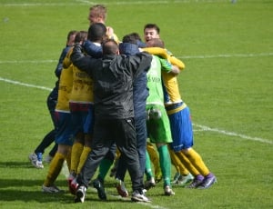 soccer players group hug on green grass field during daytime thumbnail
