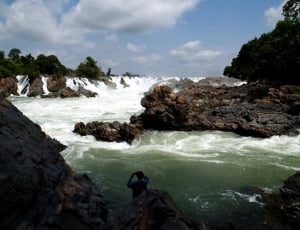 man in long sleeve shirt taking photo of river during daytime thumbnail