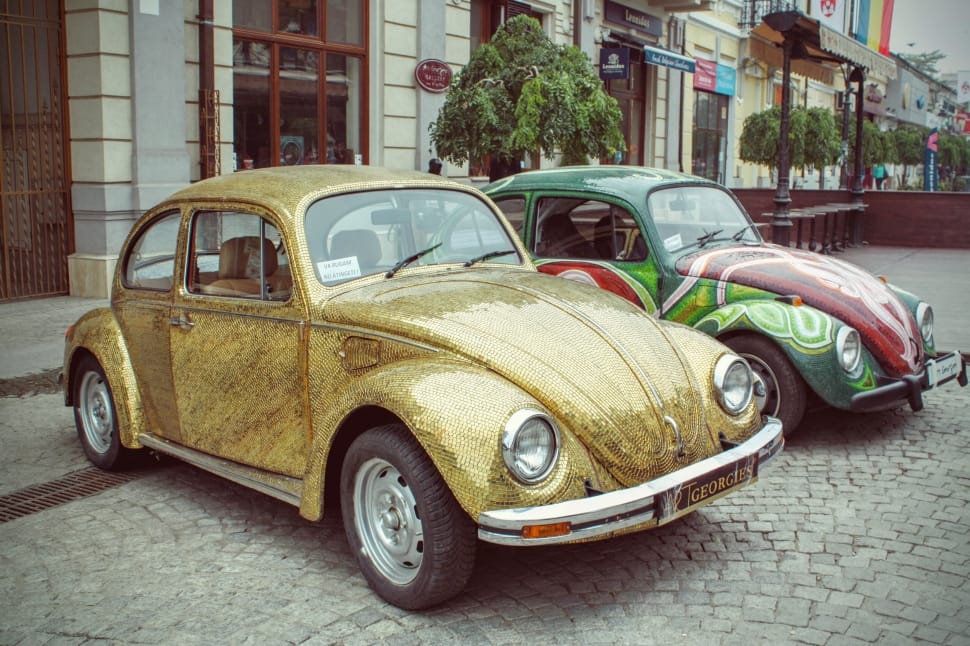 two yellow and green Volkswagen Beetle parked near on brown and gray concrete building preview