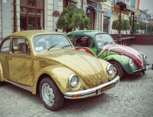 two yellow and green Volkswagen Beetle parked near on brown and gray concrete building thumbnail