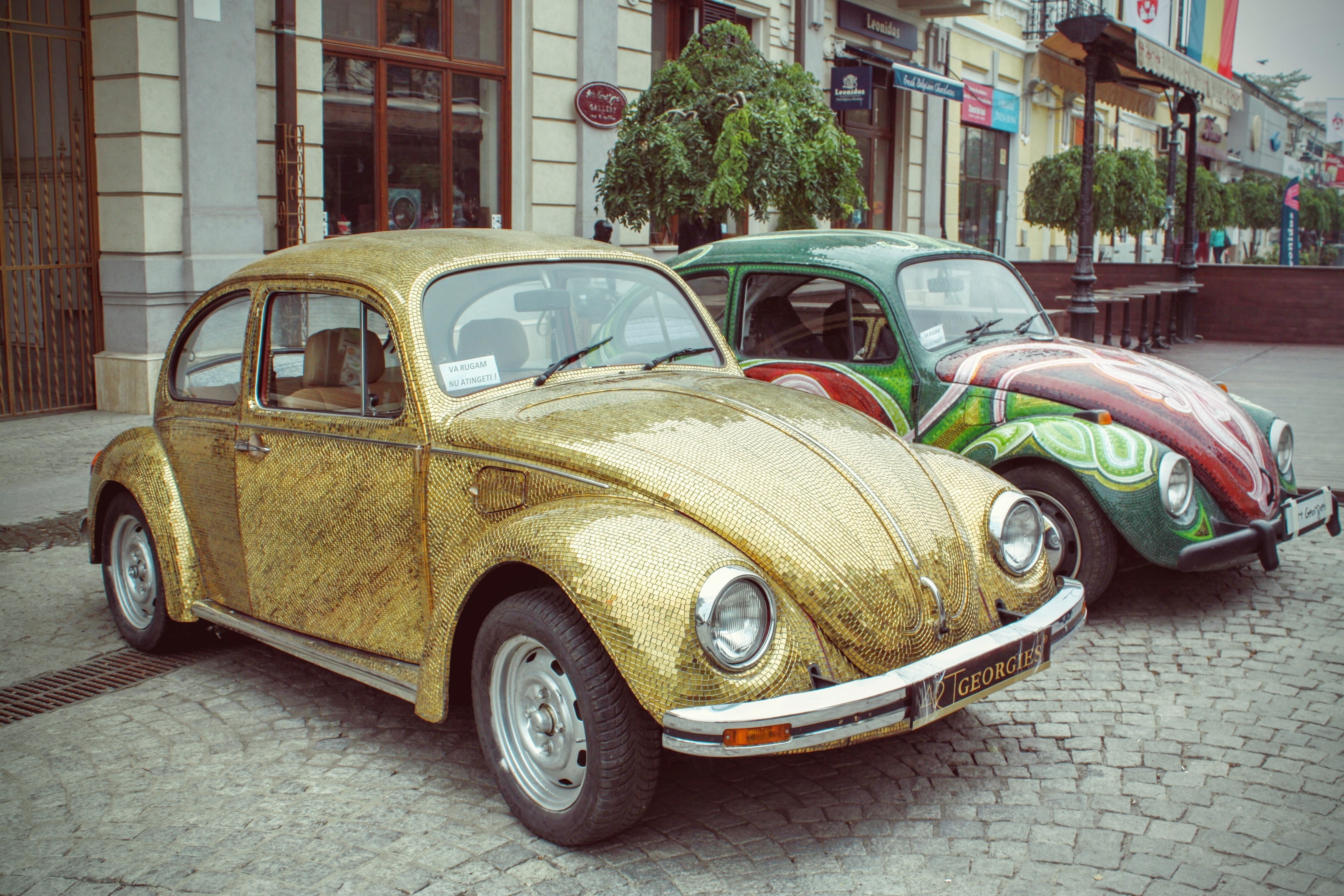 two yellow and green Volkswagen Beetle parked near on brown and gray concrete building