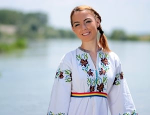 woman wearing white blue green and red printed long sleeve dress near body of water during daytime thumbnail