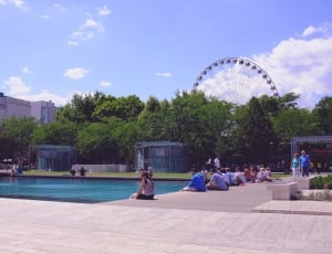 blue swimming pool; beige concrete park; green trees; beige concrete building; ferris wheel thumbnail