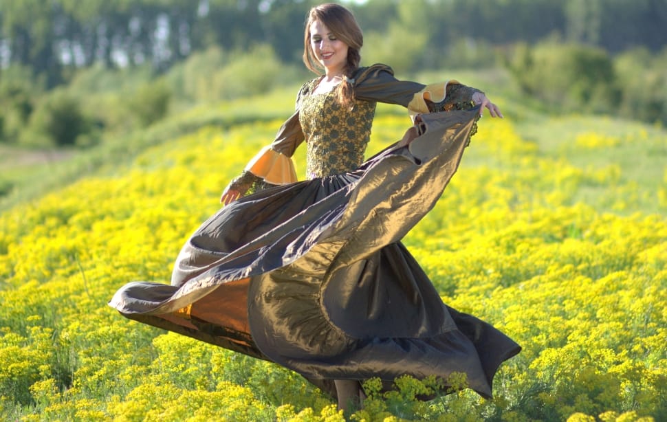 woman wearing brown and green long sleeve dress dancing on green flower field during daytime preview
