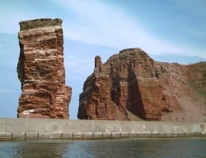 brown rock monolith next to mountain and body of water thumbnail