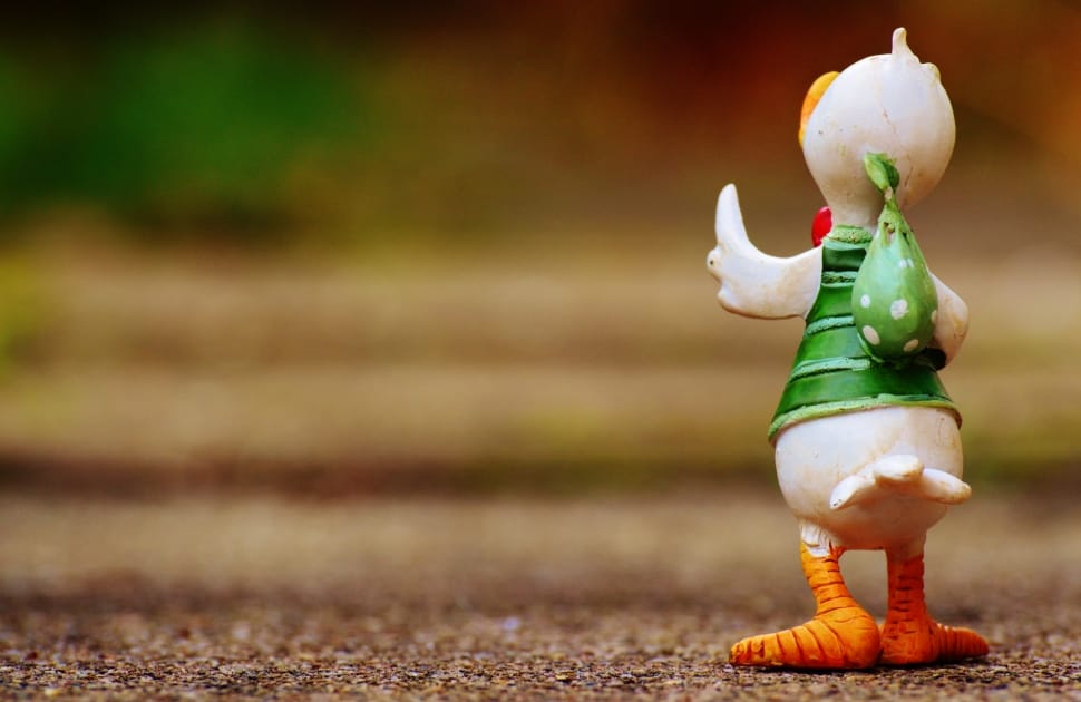 person taking photo of white, green, and orange bird figurine in tilt shift photography preview