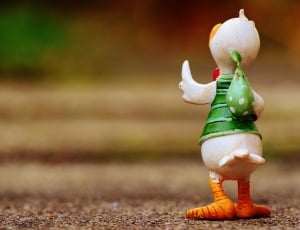 person taking photo of white, green, and orange bird figurine in tilt shift photography thumbnail