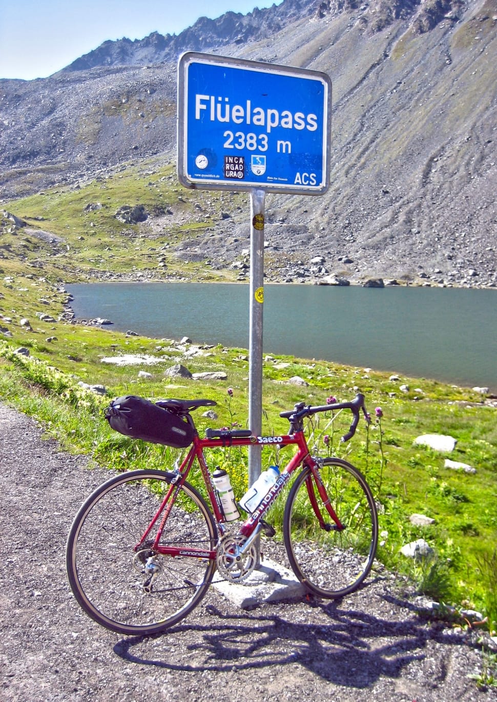 black and red road bike leaning on grey and blue Fluelapass signage near body of water preview