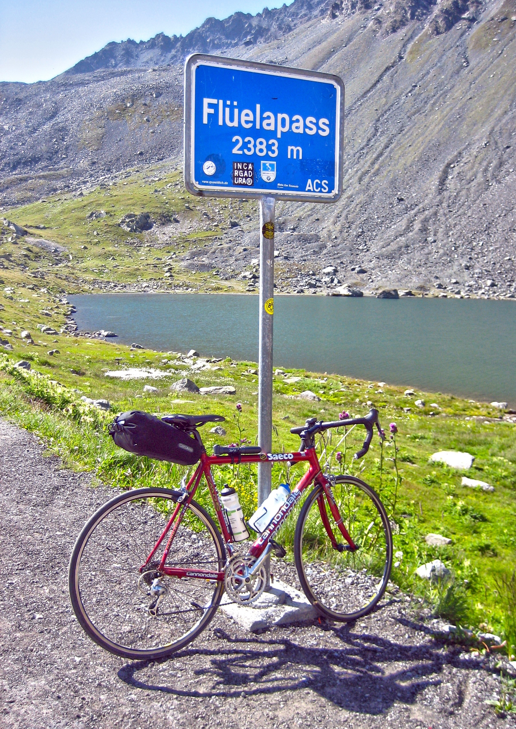 black and red road bike leaning on grey and blue Fluelapass signage near body of water