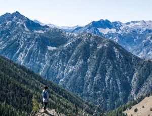 human standing on peak of mountain facing green trees and mountains thumbnail