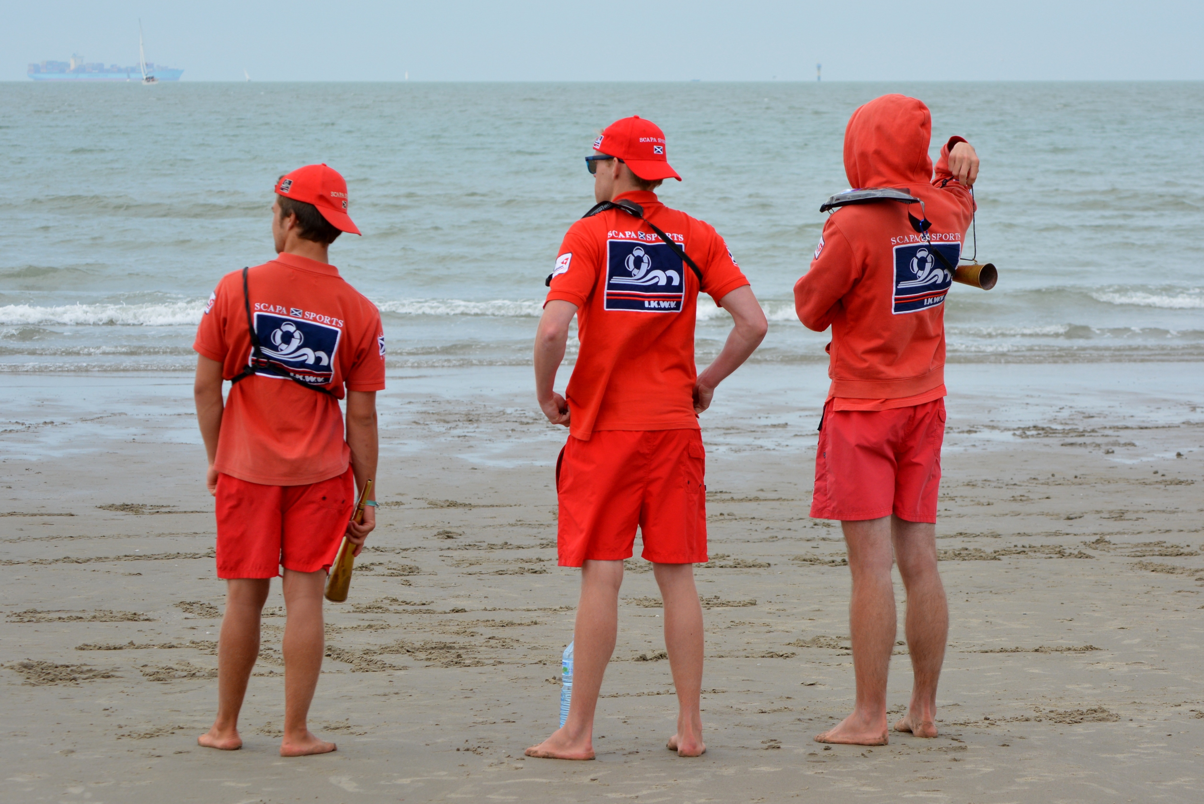 three men in red polo shirt and red shorts standing at the seashore during daytime