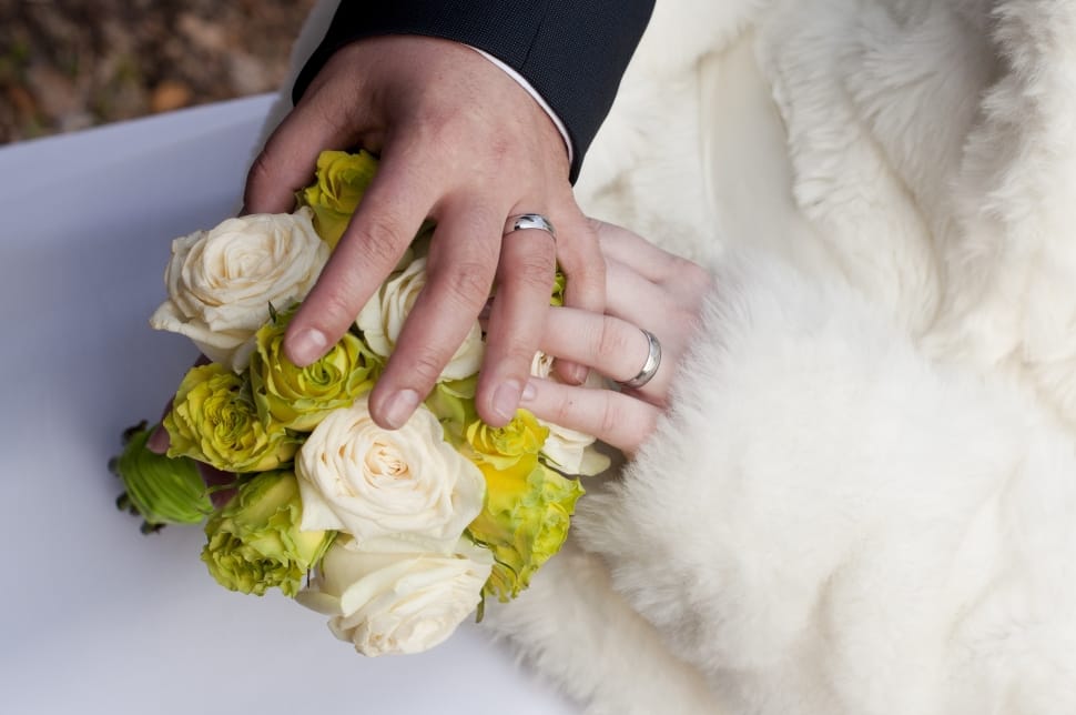 bride and groom's hands holding bouquet of white and green flowers preview