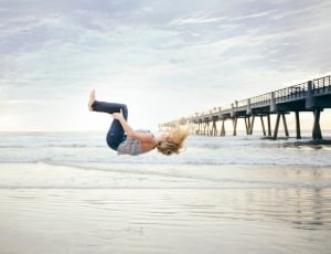 woman in black jeans and floral top back tumbling in the seashore thumbnail