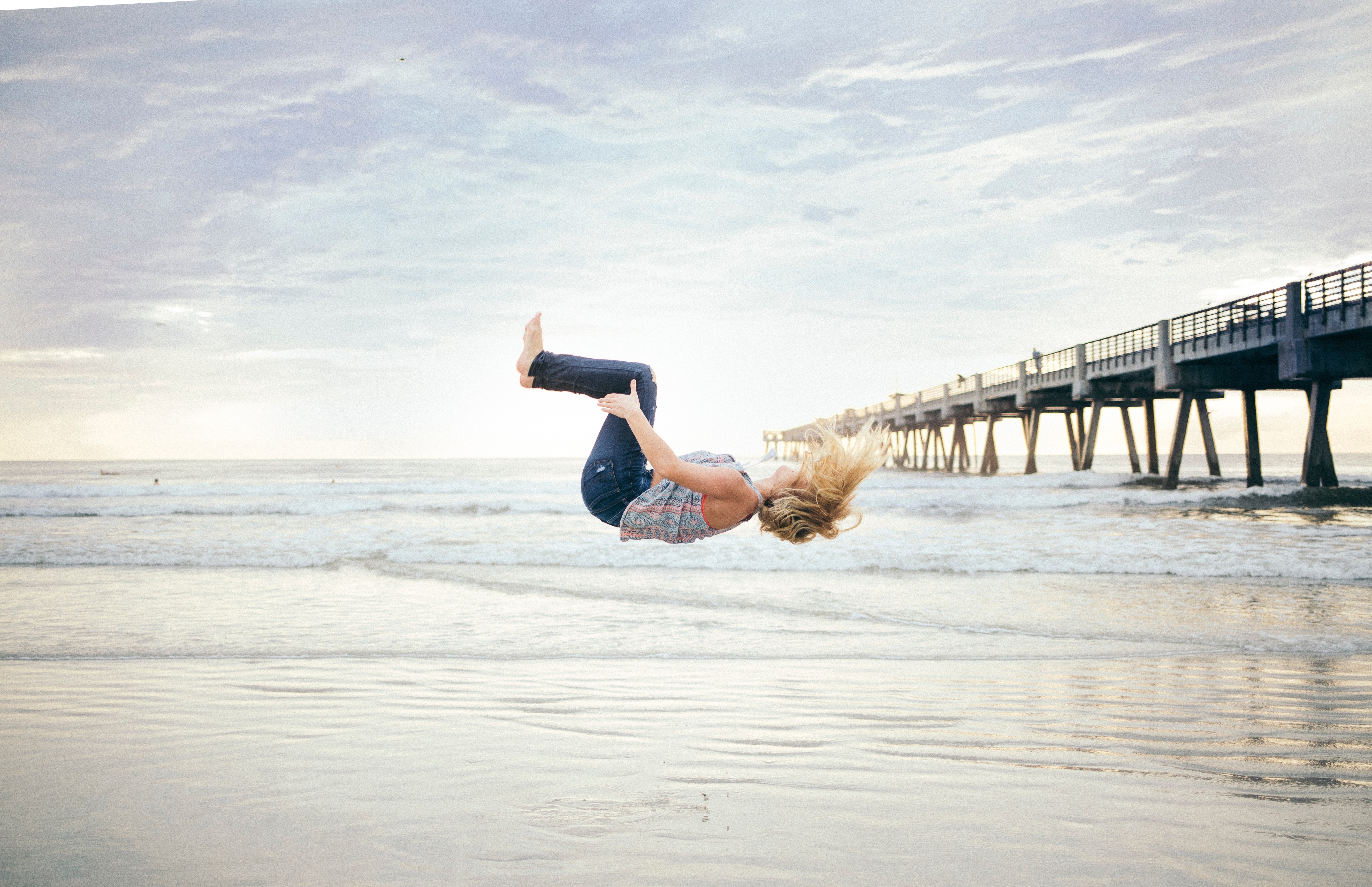woman in black jeans and floral top back tumbling in the seashore
