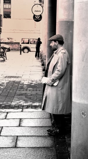man in long coat standing near the wall thumbnail
