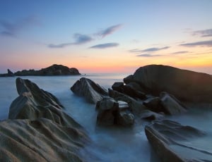 gray rock formation at blue sea under blue and yellow sky during golden hour thumbnail