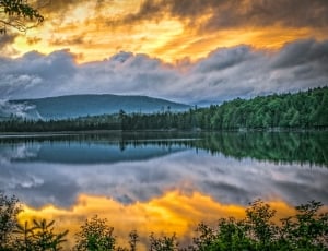 panorama photography of green trees and lake under white clouds and yellow sky during daytime thumbnail
