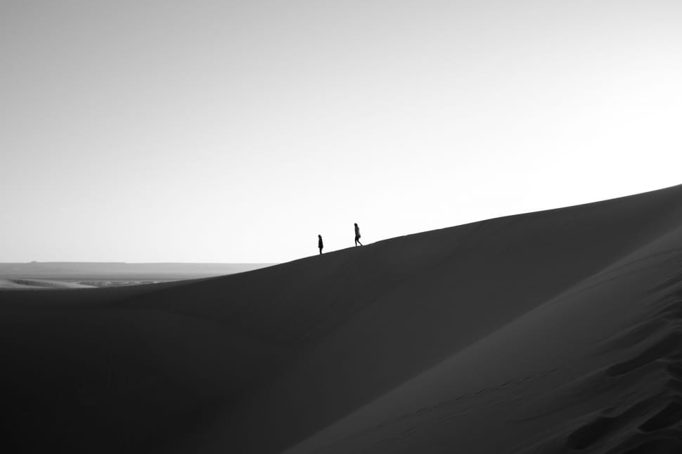 black and white picture of two person walking through mountain dessert preview