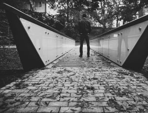 grayscale photo of a man standing in a bridge thumbnail