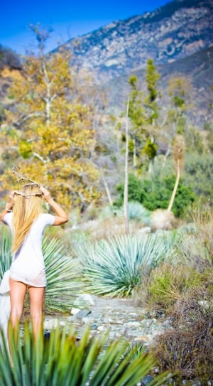 woman in white t shirt putting on twig headband standing near bushes during daytime thumbnail
