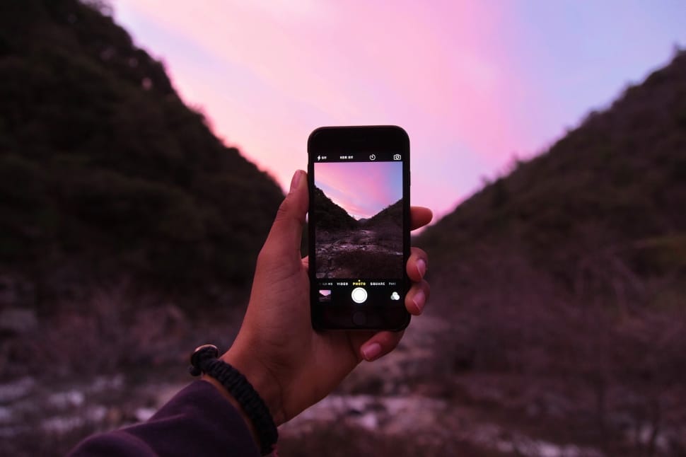 left human hand holding a black smartphone during sunset preview