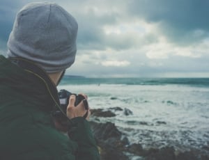 man holding camera in front of body of water during daytime thumbnail