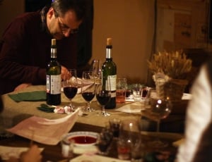 person leaning table with bottles and wine glasses thumbnail