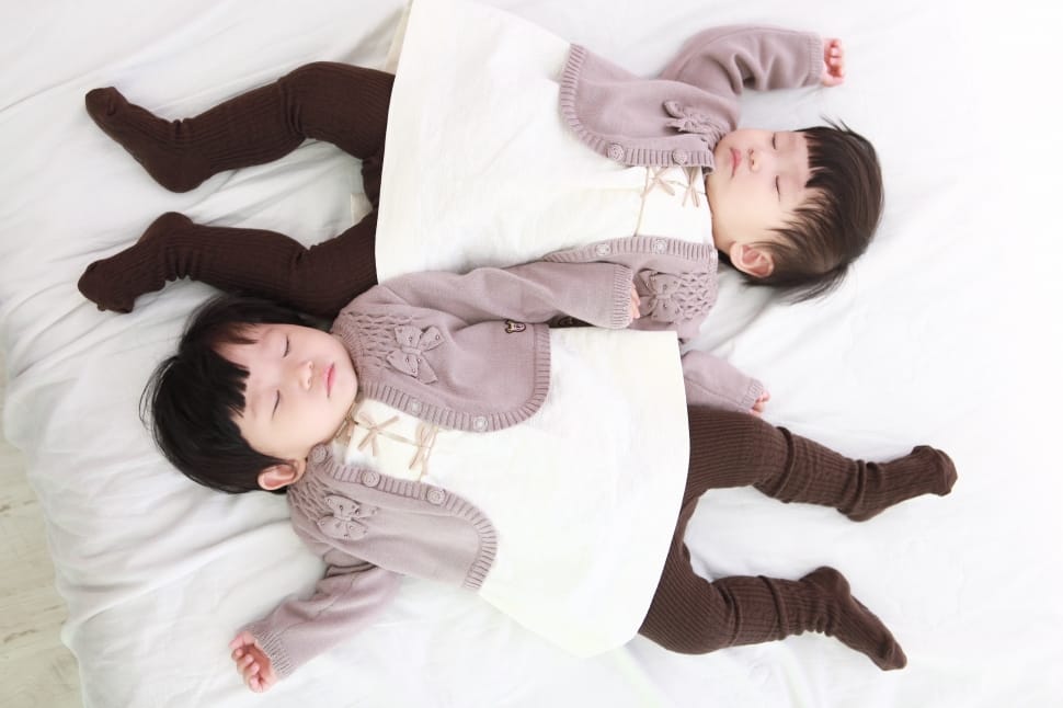 two babies in gray cardigan sleeping on a white blanket preview