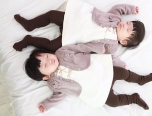 two babies in gray cardigan sleeping on a white blanket thumbnail