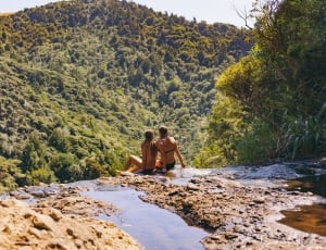 2 women wearing two piece bikini sitting on cliff at daytime thumbnail