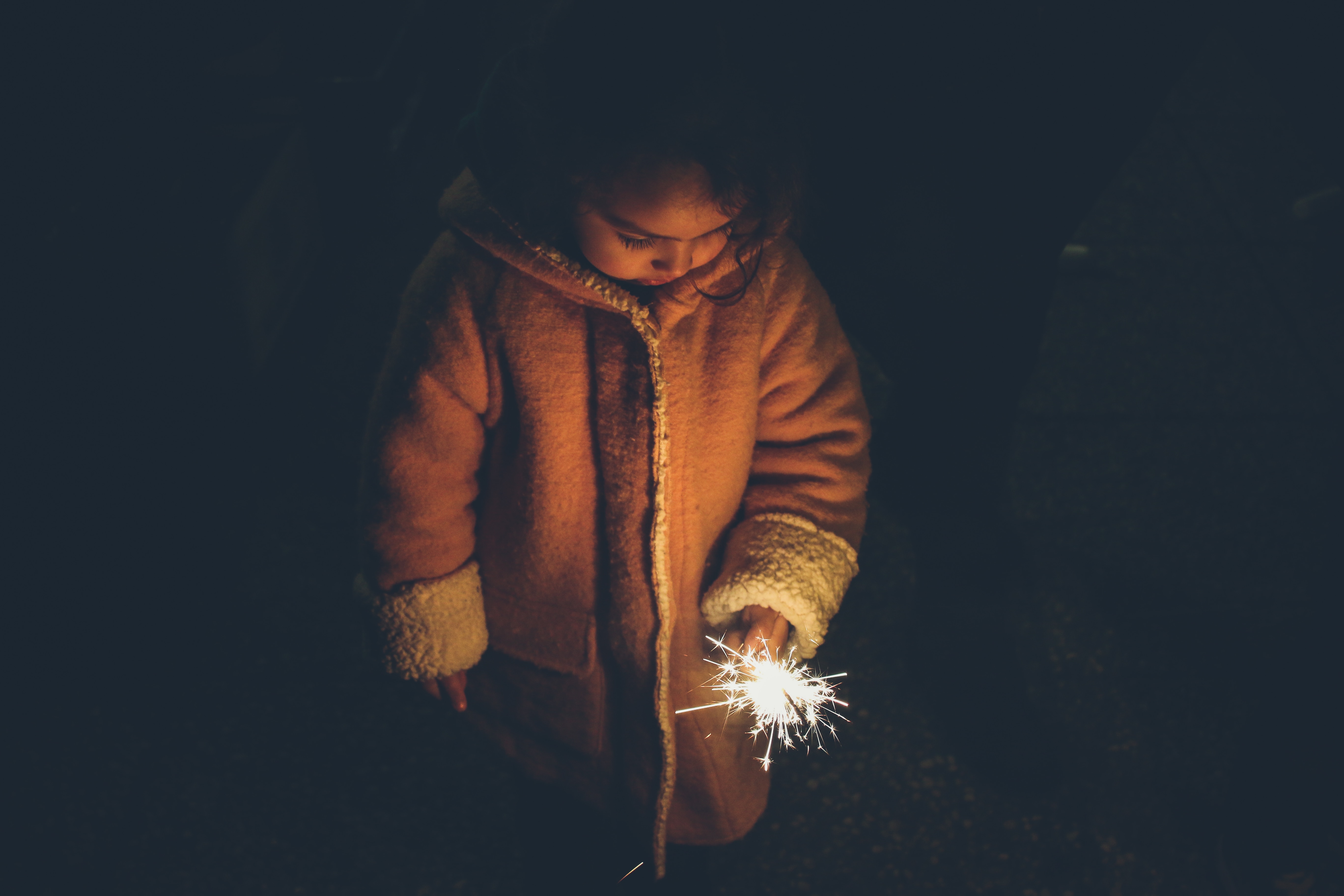 girl in brown jacket holding sparkles fireworks